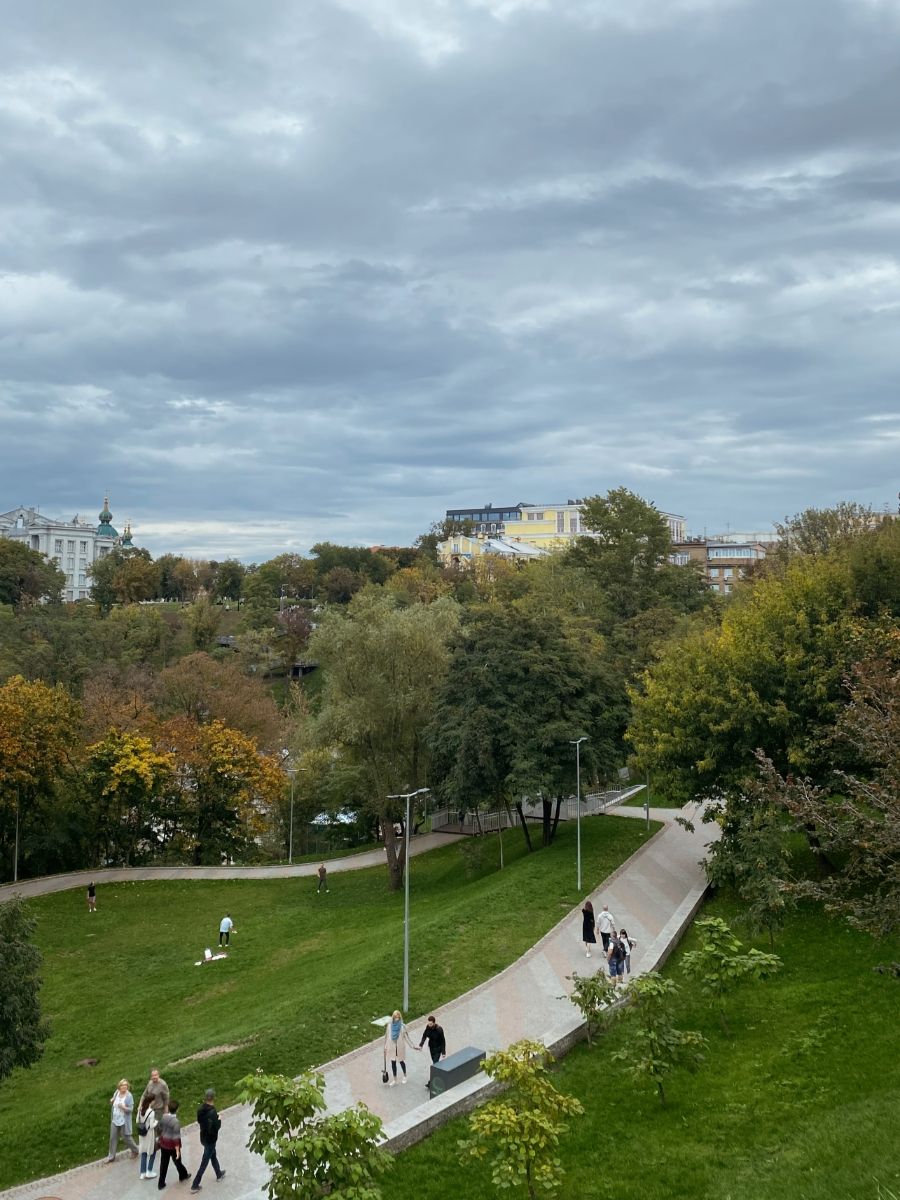 People walking in a park with cloudy skies and colorful autumn trees.
