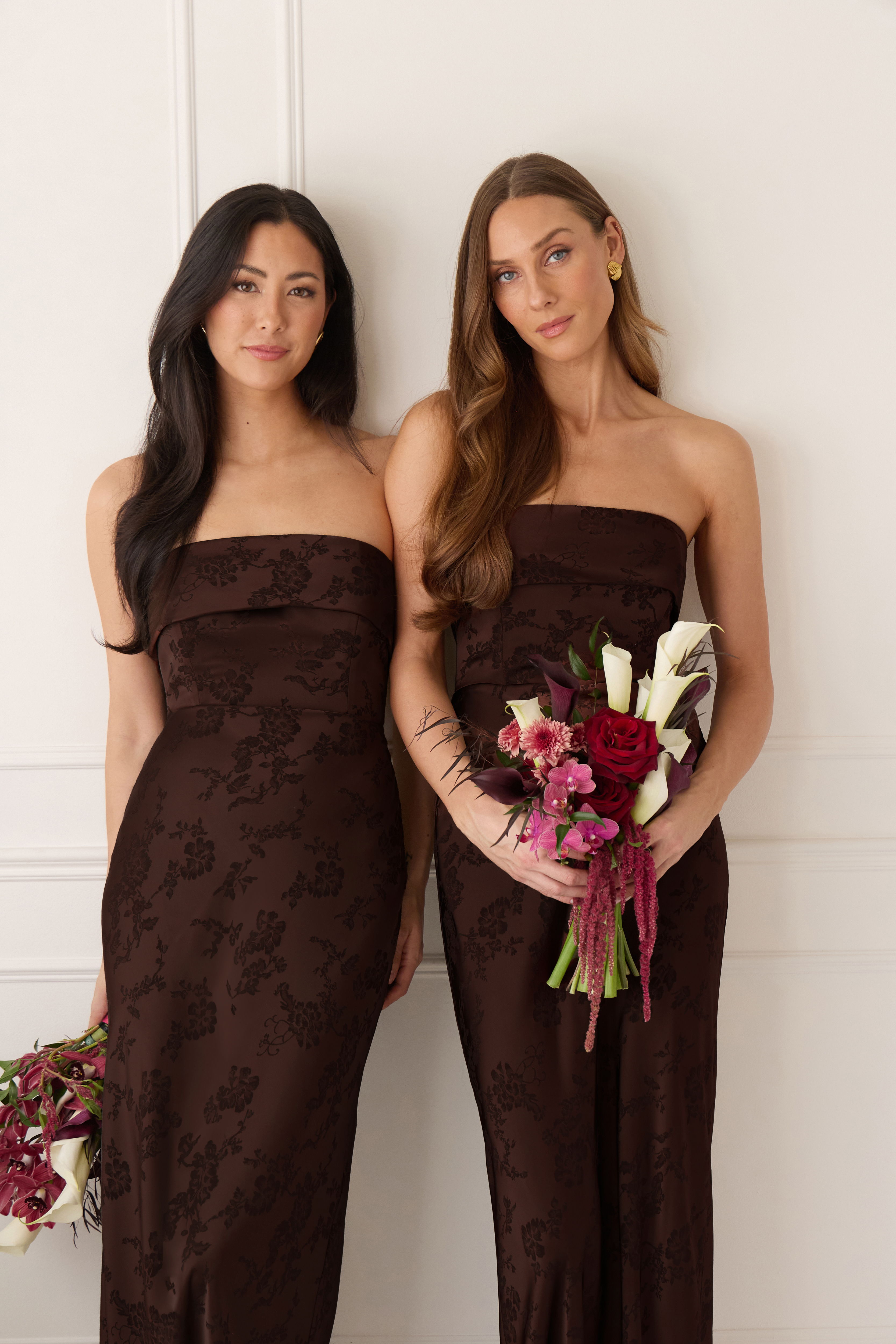 Two women in brown strapless dresses holding bouquets.