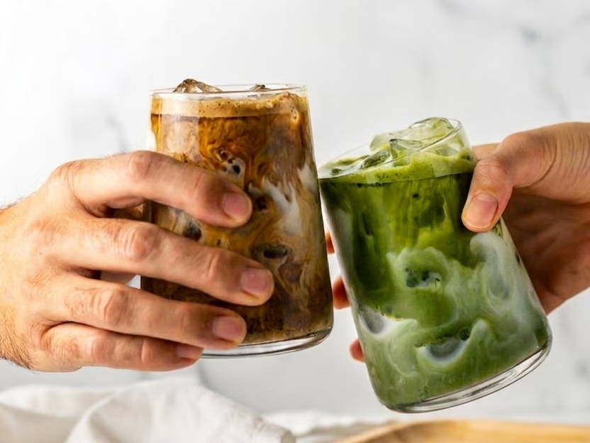 Two hands clinking glasses ofRoasted Matcha Latte and Matcha Latte