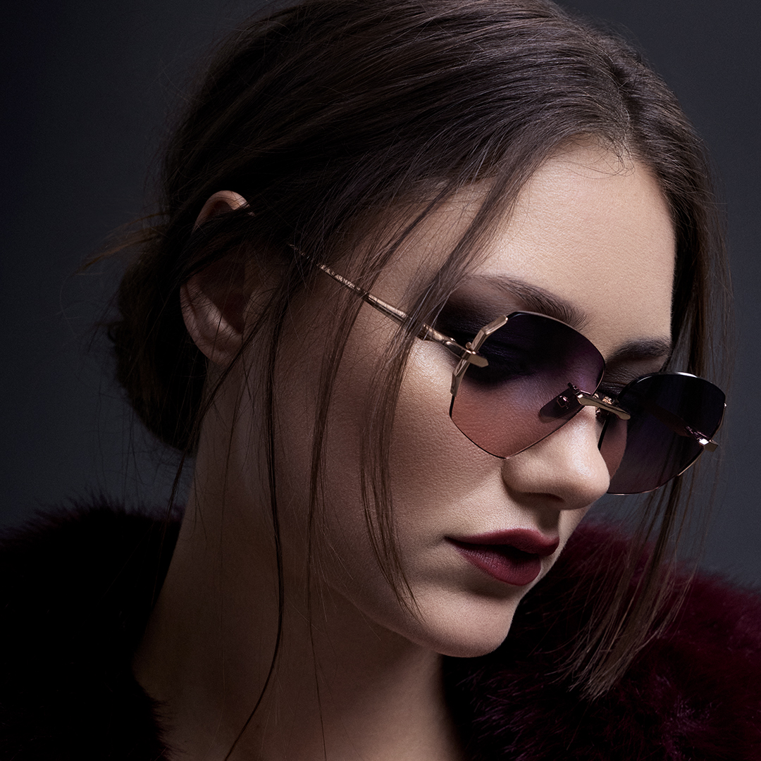 Woman wearing sunglasses with dark background and stylish attire.