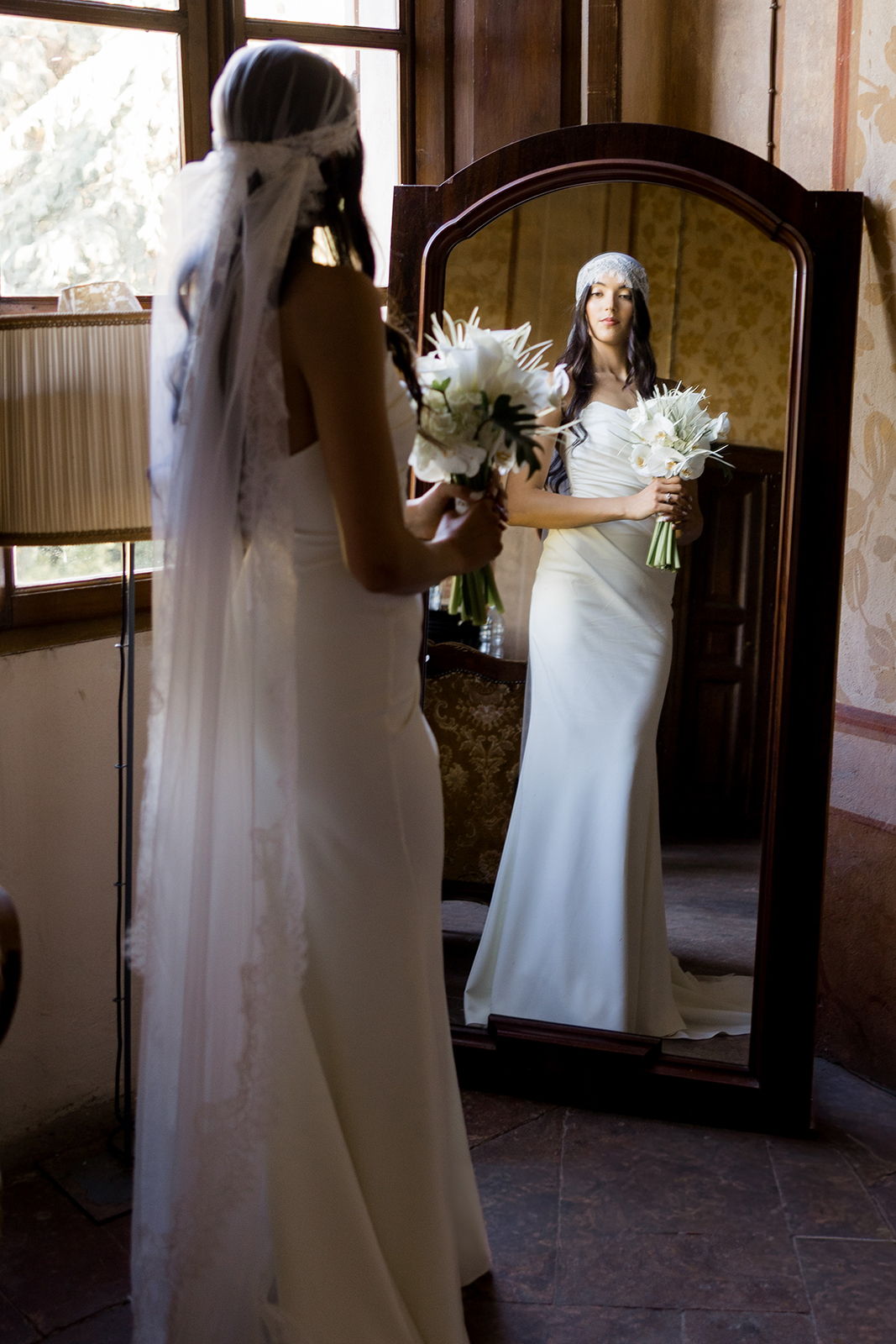 Bride in wedding dress holding flowers, reflected in a mirror.