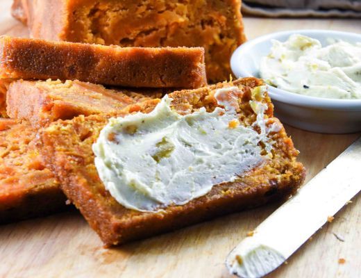 Sliced bread with cream cheese spread and a butter knife on a wooden surface.