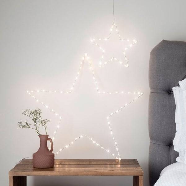 2 Osby star lights one hanging on the wall and one on the side table of a bed.