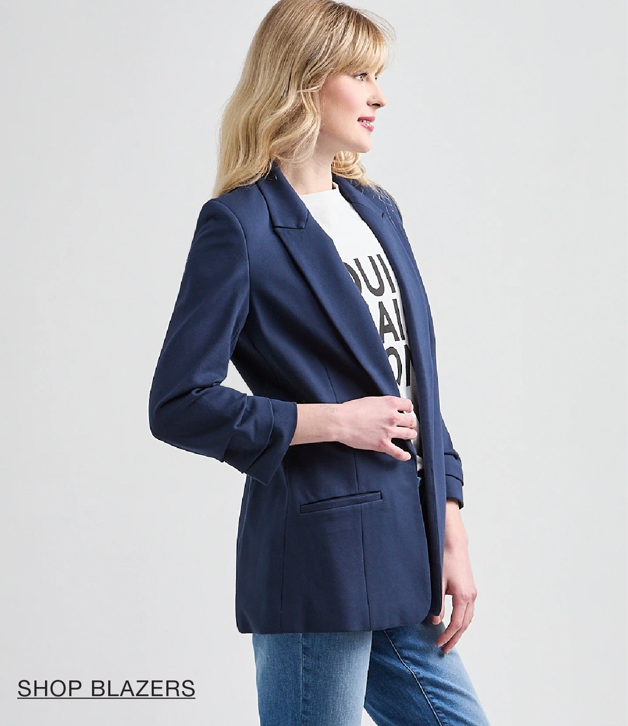 Woman in a navy blazer and graphic t-shirt, posing sideways.