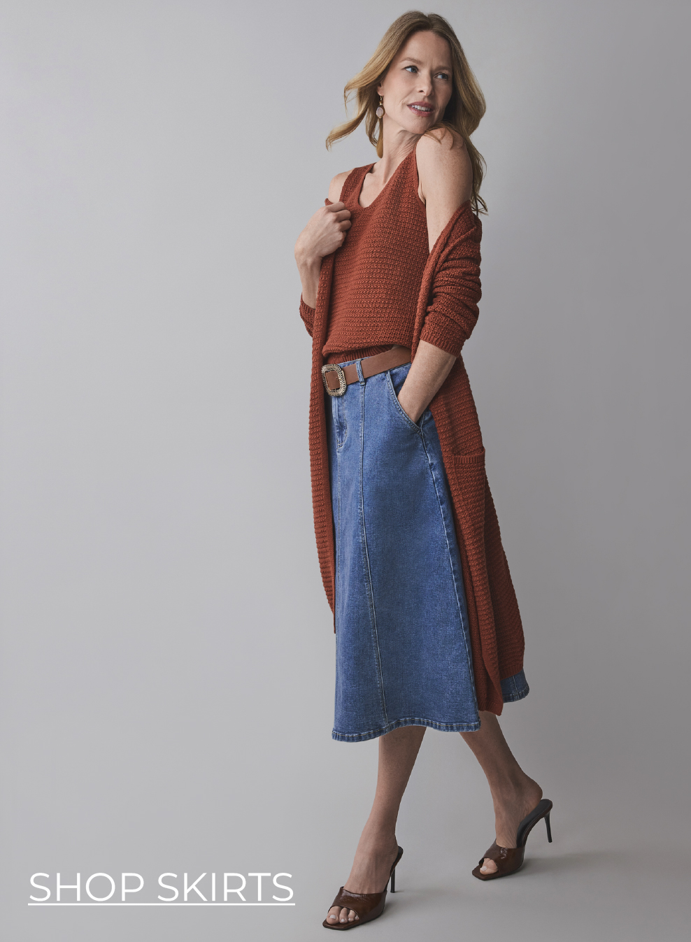 Woman wearing a brown top and blue skirt, posing confidently.