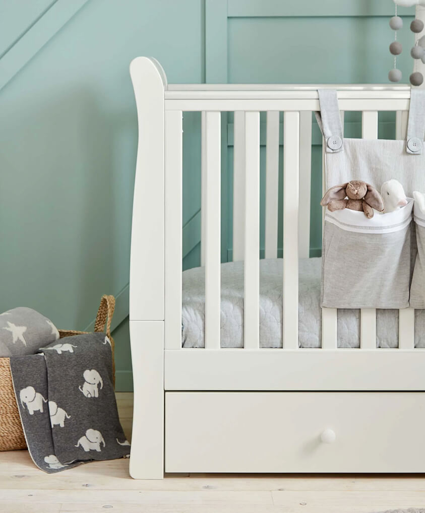 A white cotbed with soft bedding and a decorative blanket nearby.