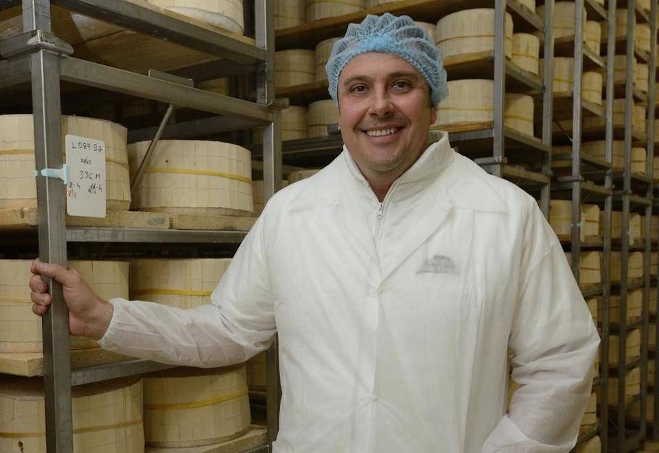 Artisan Gorgonzola maker stands smiling by stacks of his cheese