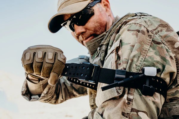 Soldier in tactical gear adjusting equipment outdoors.