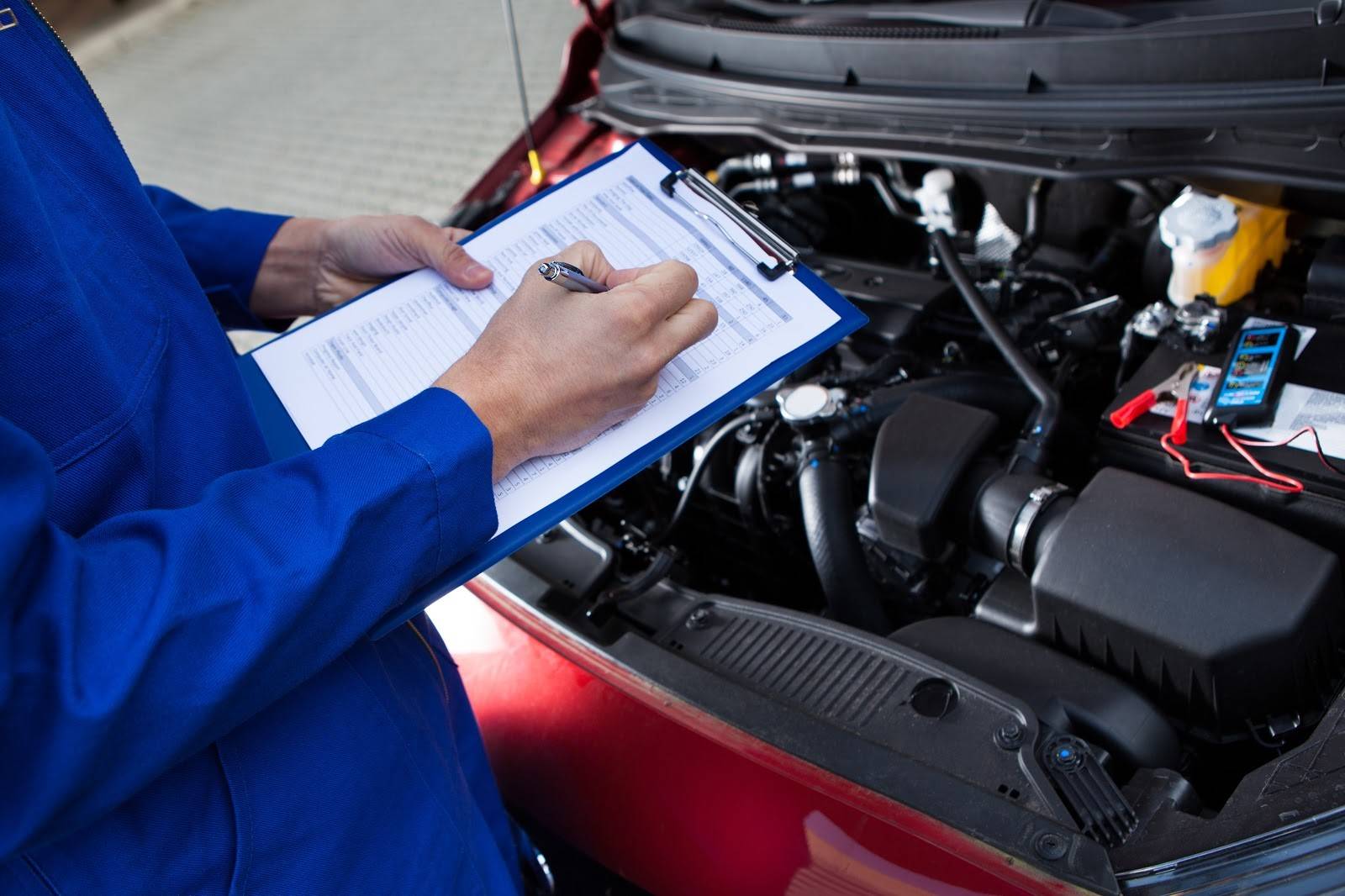 A mechanic reviewing a car maintenance checklist and observing an engine