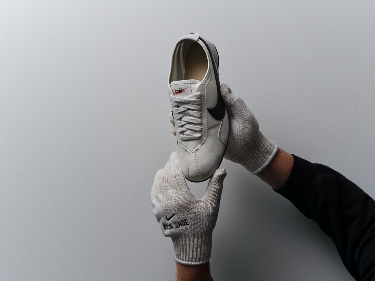 A person holding a white Nike shoe against a neutral background.