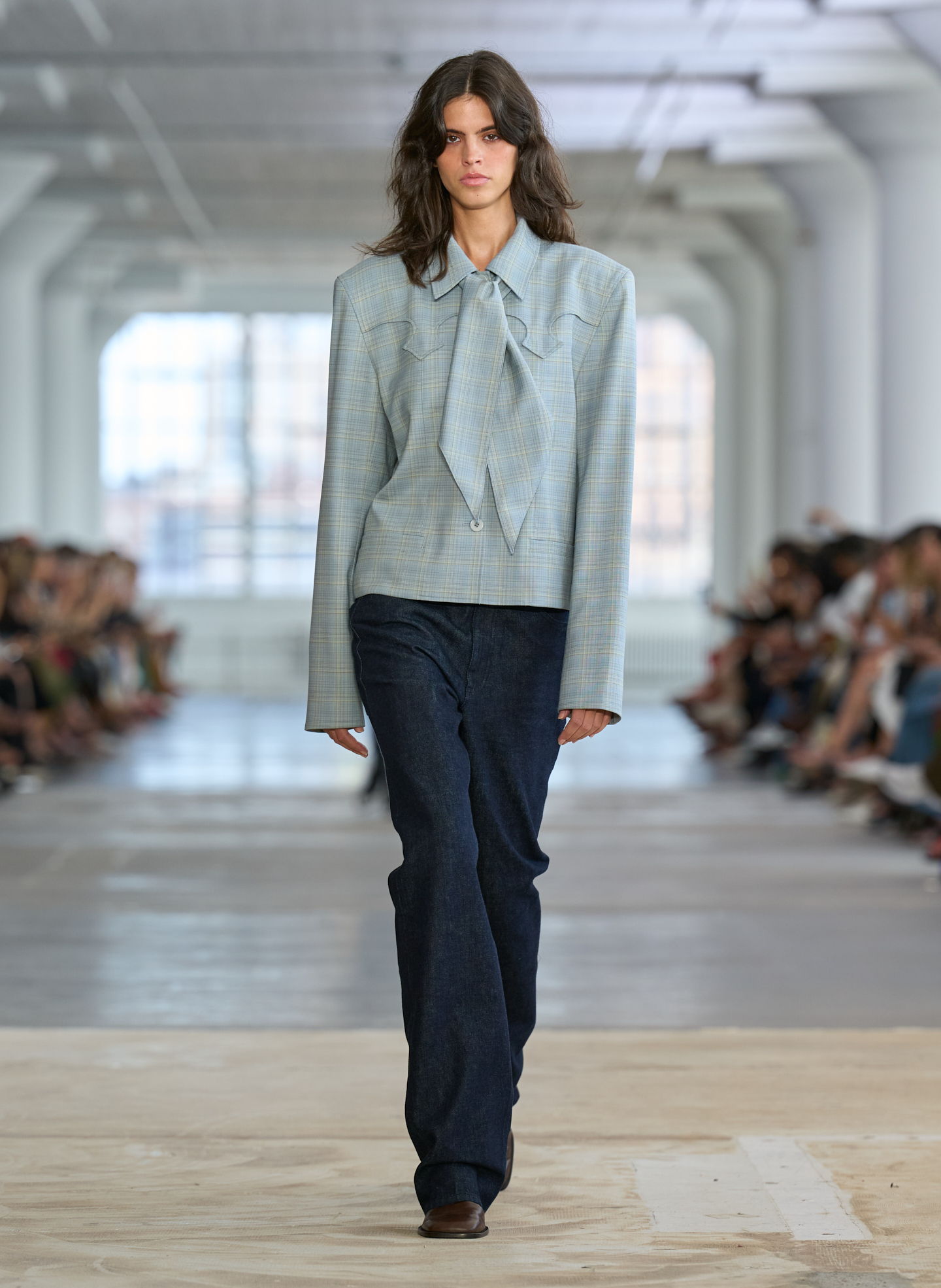 Model walking down runway in stylish outfit during fashion show.