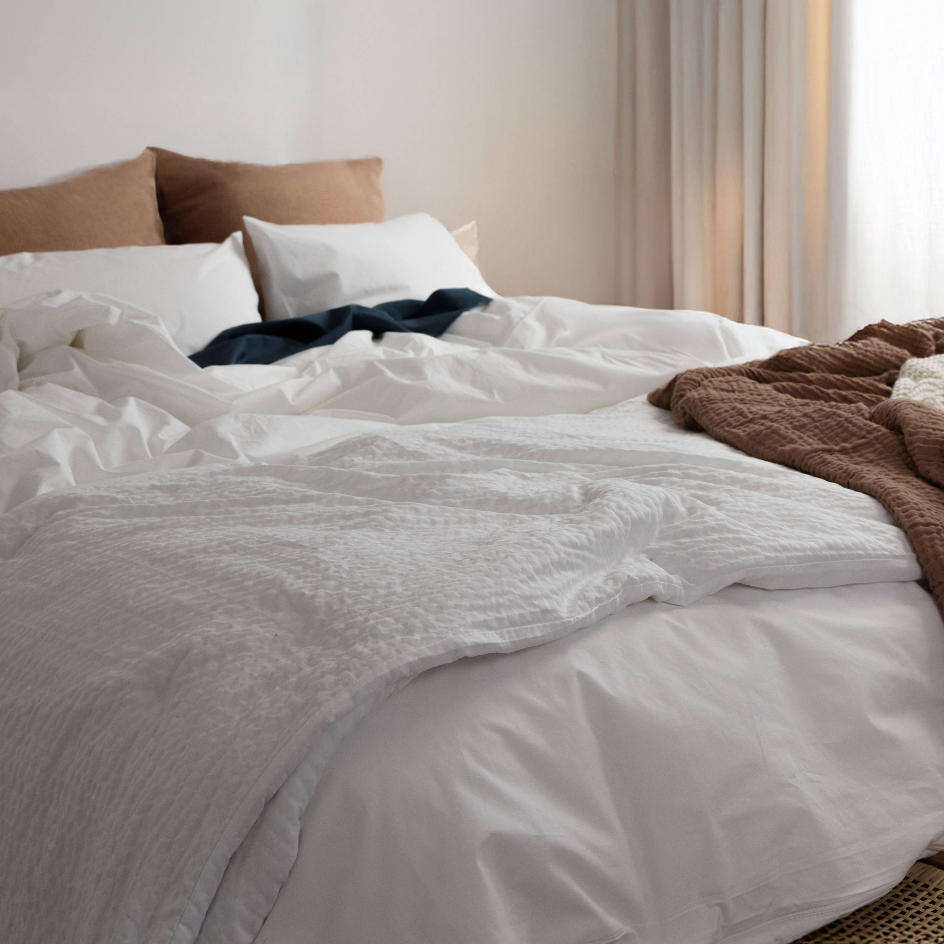 rumpled bed with white percale bedding-pillows-rust and ivory throws and white cumulus blanket