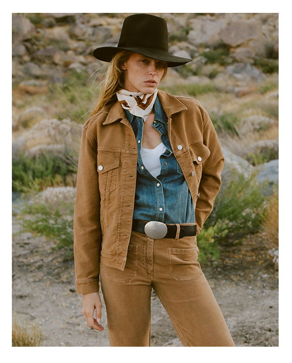 A woman in a cowboy hat poses in a rustic outdoor setting.