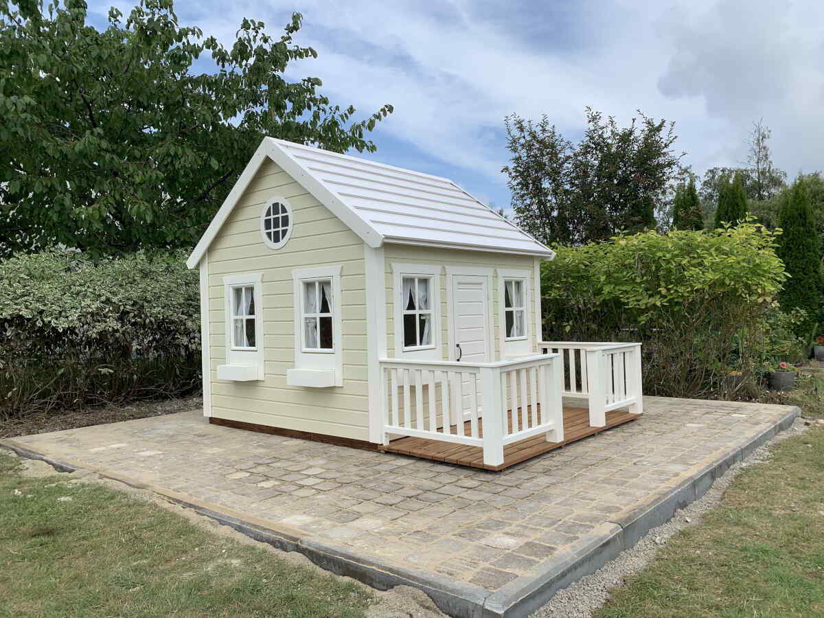 Beige custom wooden playhouse with white features and a terrace on a green background by WholeWoodPlayhouses