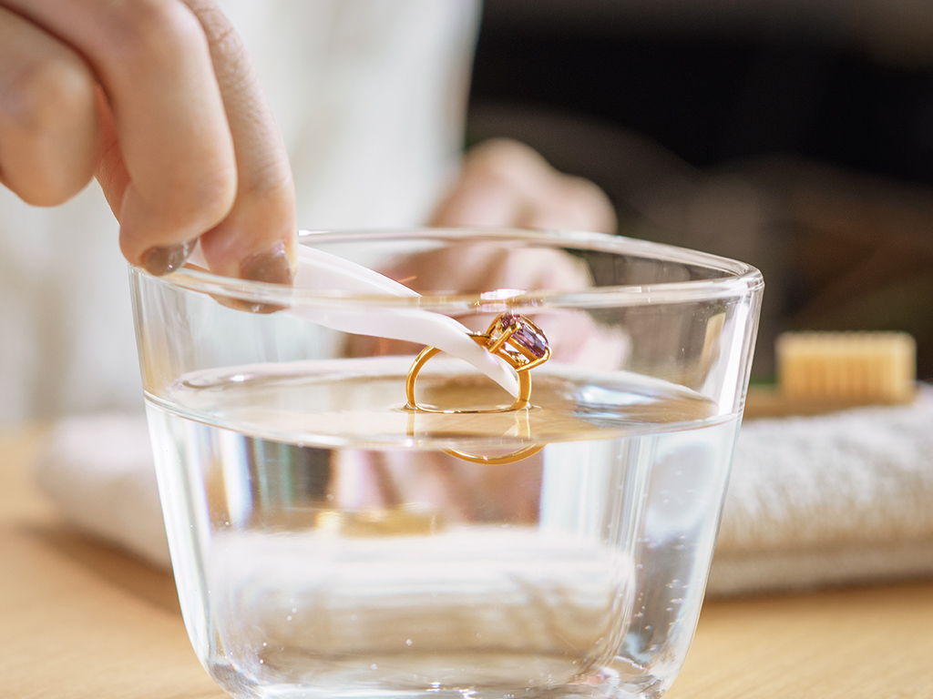 A person cleaning a ring in a glass of water.