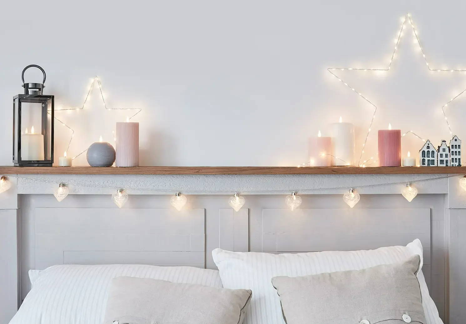 A cosy bedroom setting with stars, fairy lights and candles above a bed.