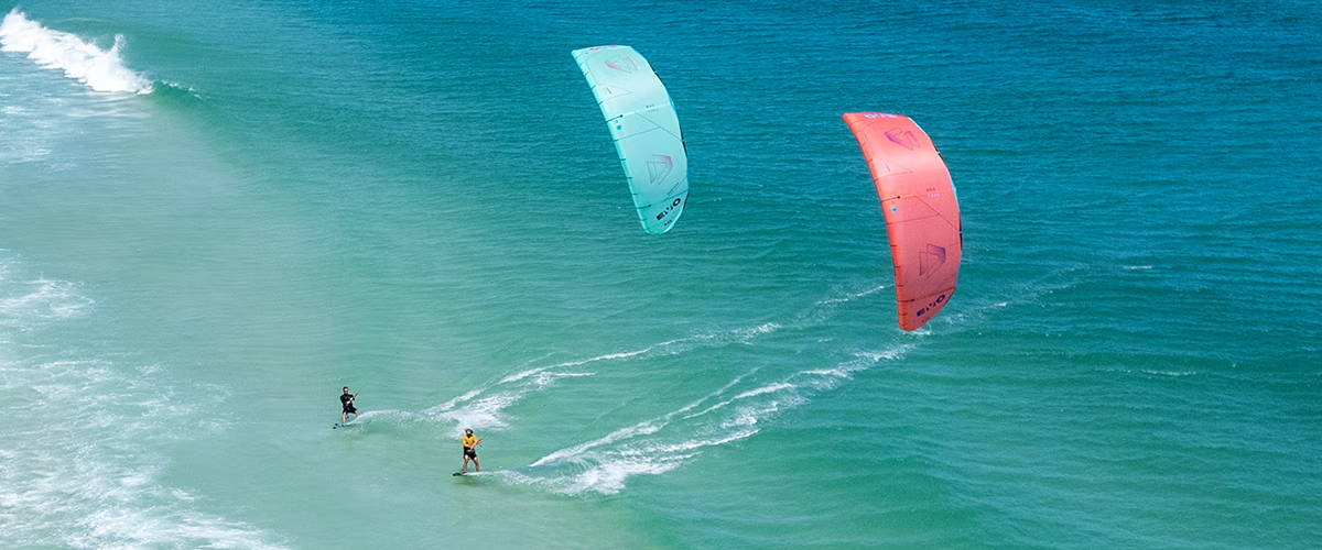 Two kitesurfers riding the waves with colorful kites at the beach.