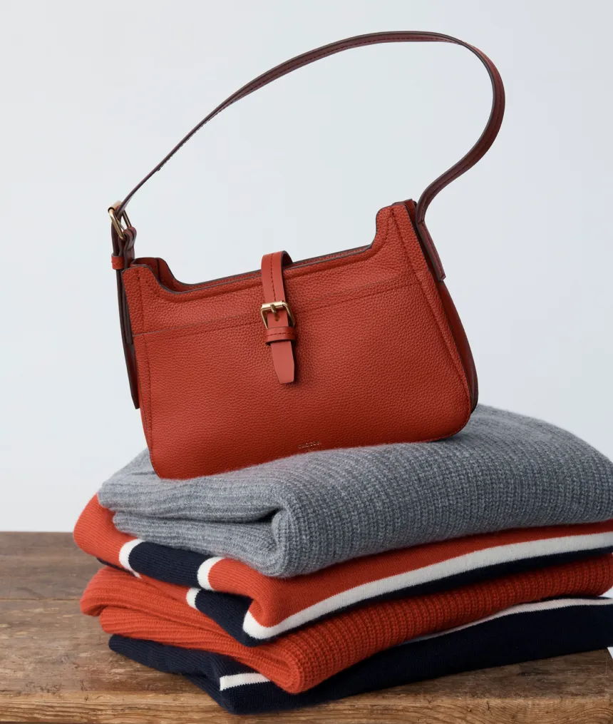 A brown handbag on top of folded sweaters.