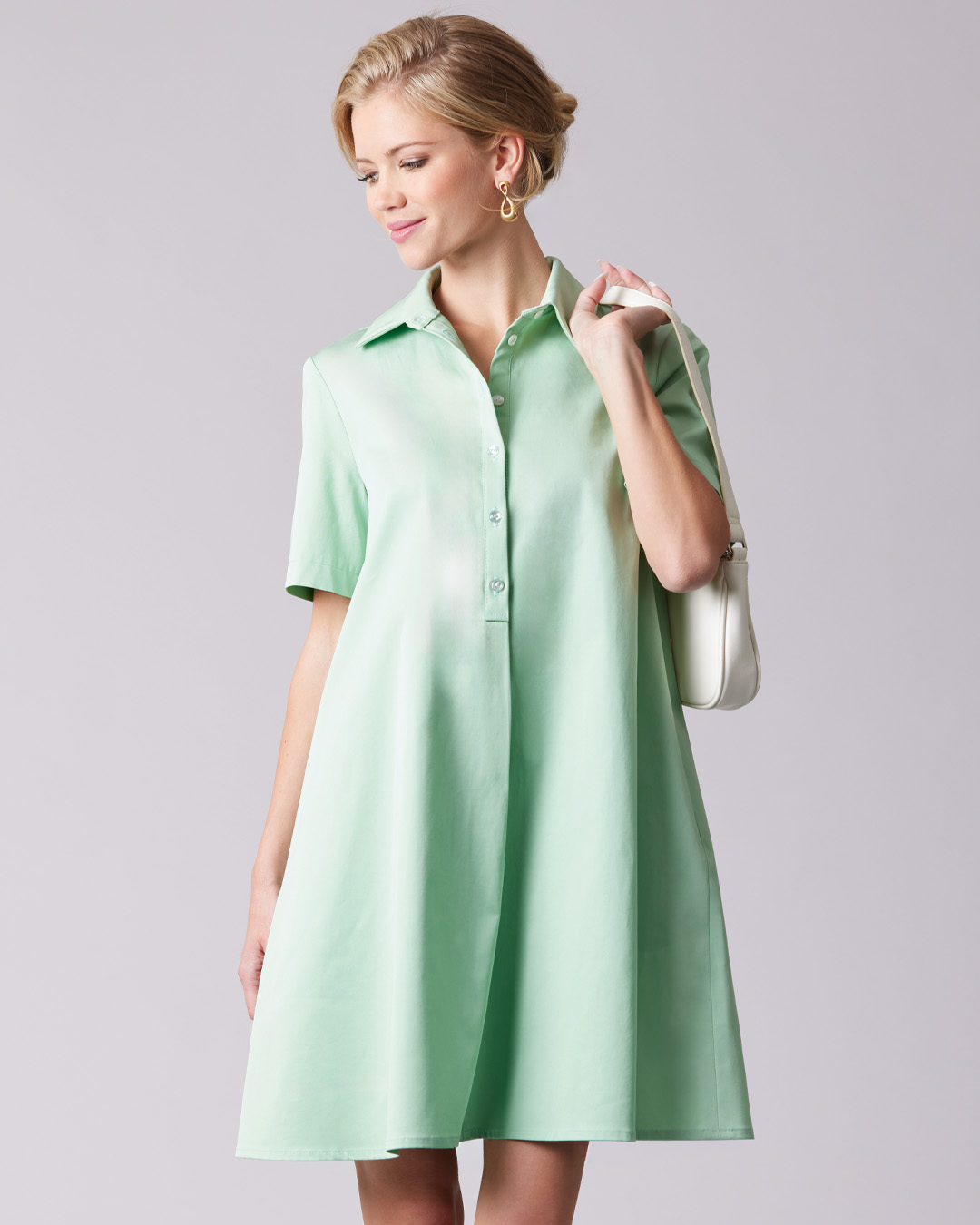 Woman wearing a short-sleeved mint green dress, holding a white handbag.