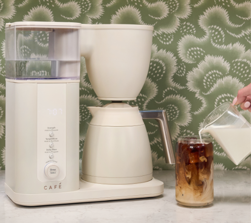 Coffee maker brewing iced coffee with milk being poured into a glass.
