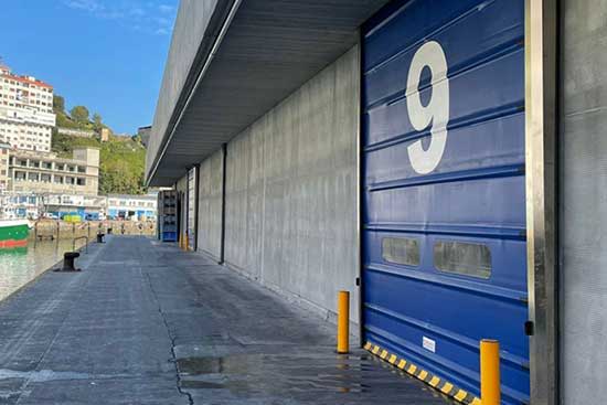 Blue garage door with the number 9, concrete wall, and clear sky.