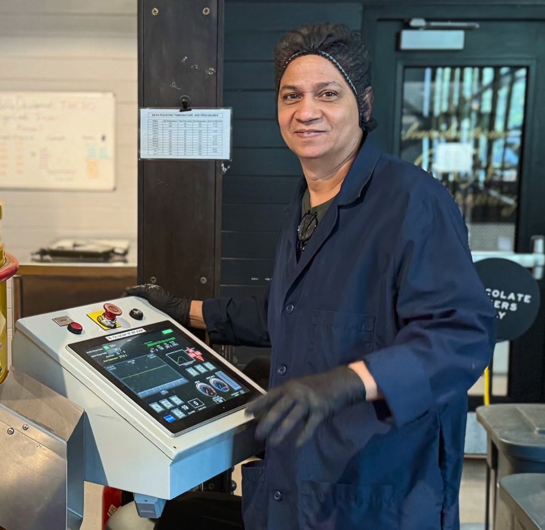 Person operating a machine, wearing gloves and a dark coat, smiling.