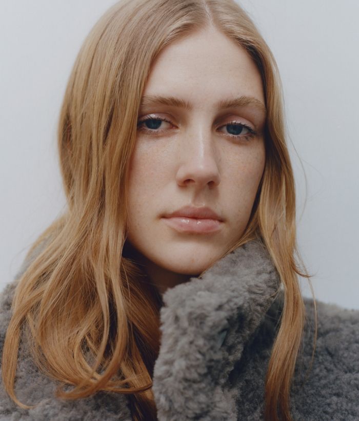 A young woman with long hair wearing a fuzzy coat, looking directly at the camera.