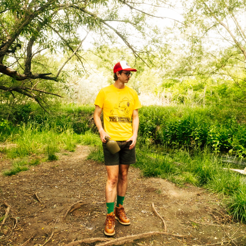 Person in a yellow shirt and red cap standing in a lush, green area.