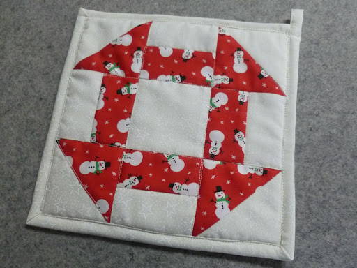 a finished handmade churn dash quilt block that is also a pot holder made from a christmas fabric