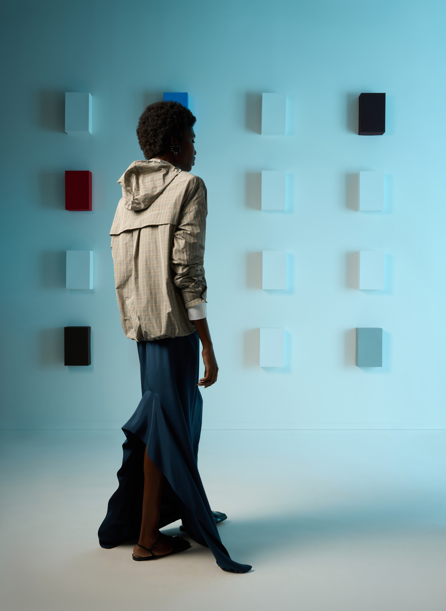 A person in fashion clothing walks near a wall of colorful panels.