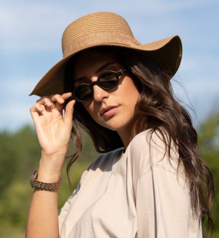 Woman wearing Magnolia, Small Round Zebrawood Sunglasses with Grey Polarized Lens with a beige shirt and a straw hat