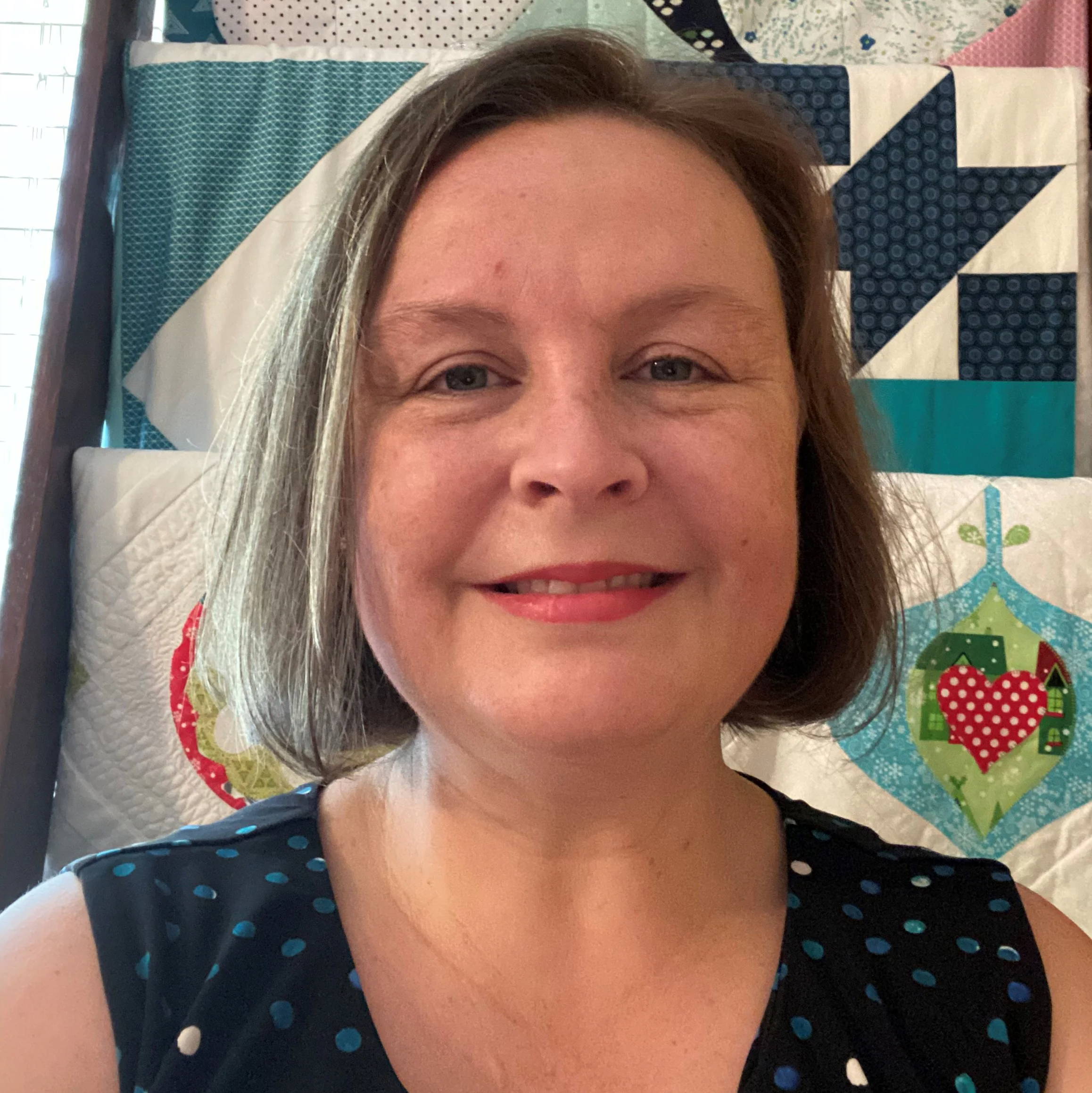 Woman smiling in front of a colorful quilt backdrop.