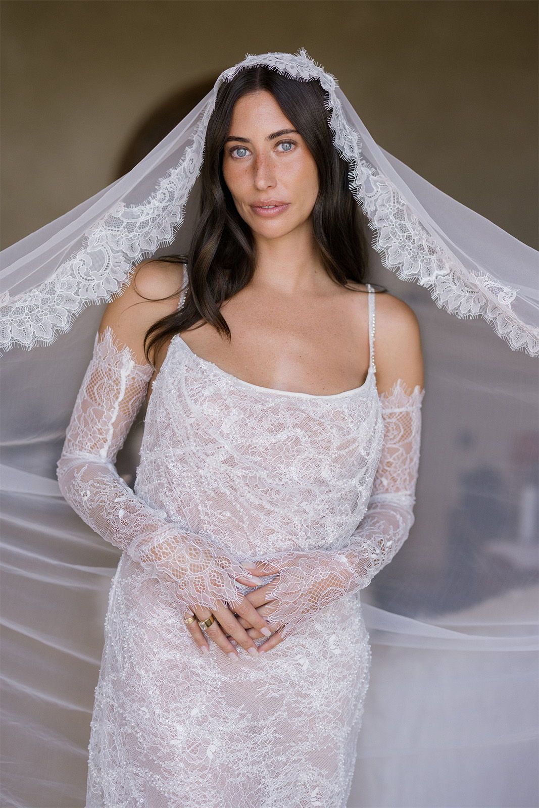 Bride in lace dress and veil, looking directly at the camera.