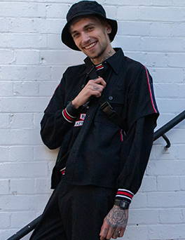 Blonde man  smiling in black bucket hat, black vintage shirt and black vintage trousers