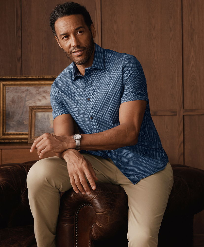 Man sitting on a couch, wearing a blue shirt and beige pants.