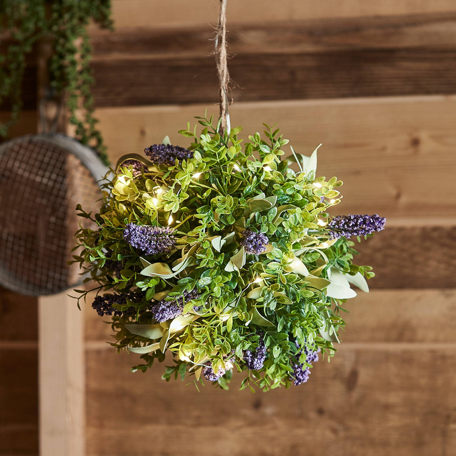 An artificial lavender topiary ball with micro lights in a wooden room.