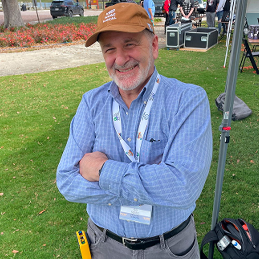 Smiling man in a cap with arms crossed, standing on grass.
