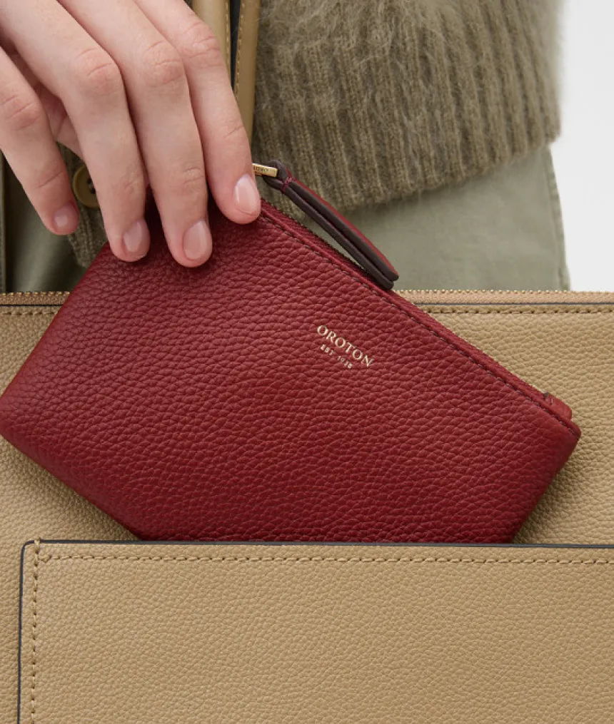 A hand placing a red wallet into a beige bag.