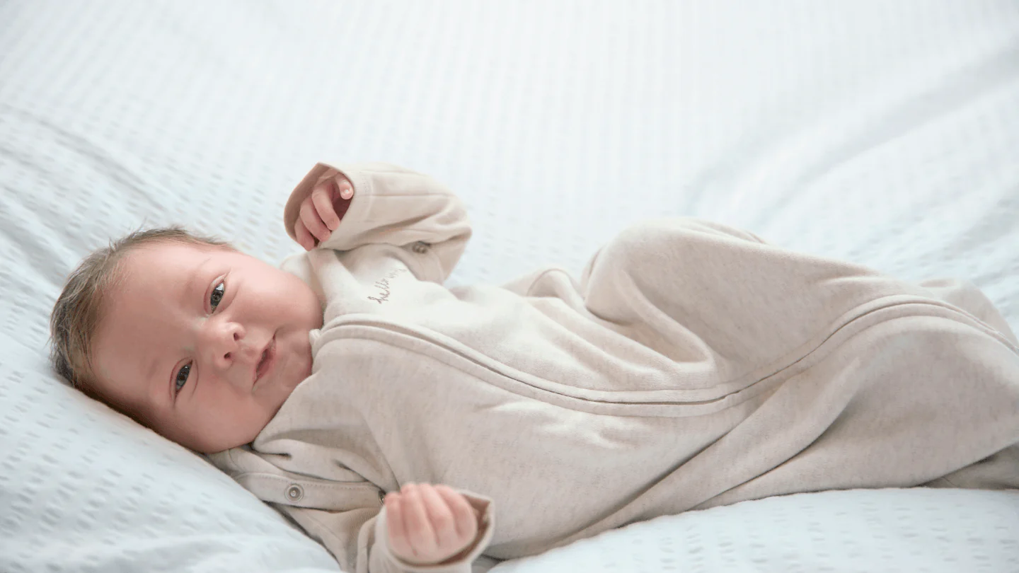 A baby lying on a soft surface, wearing a light-colored outfit.