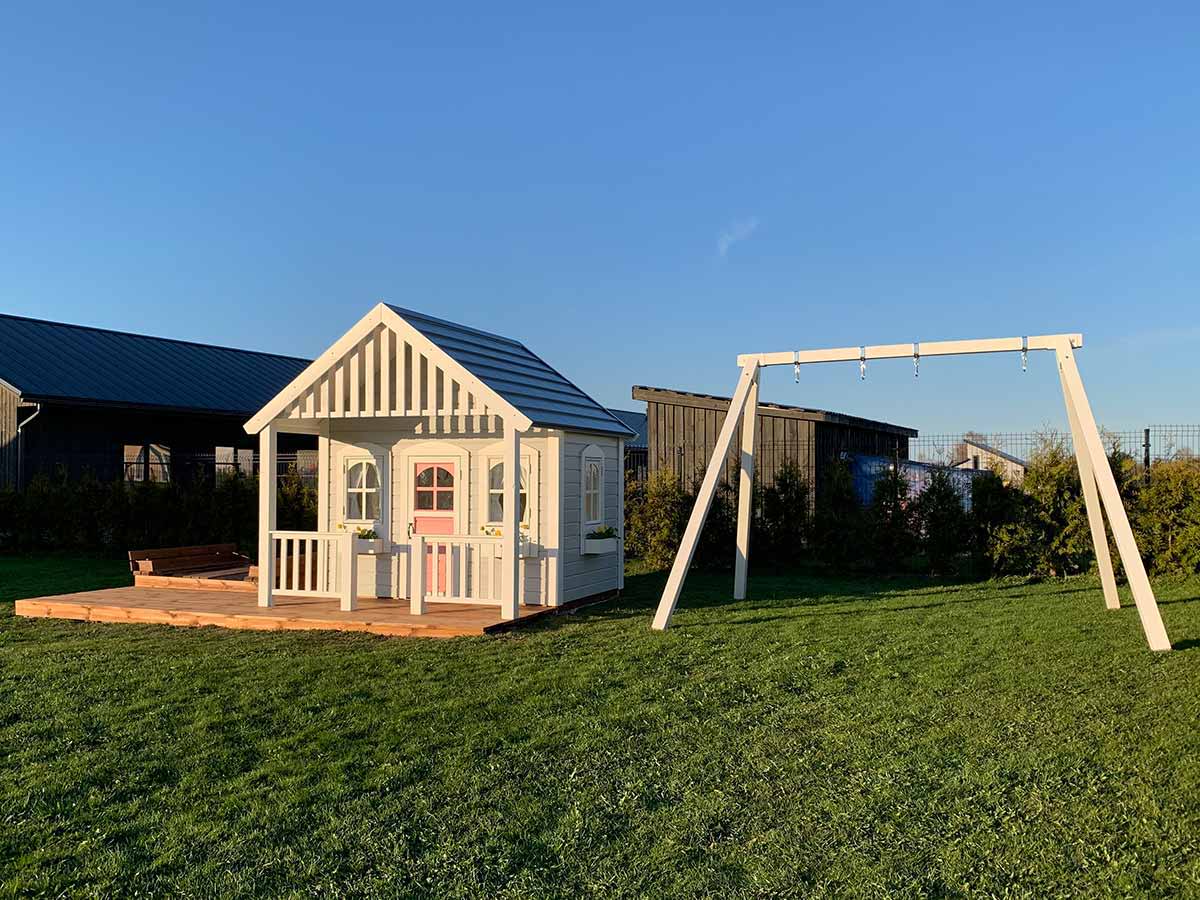 Custom wooden playhouse with white flower boxes, pink door and swing set by WholeWoodPlayhouses