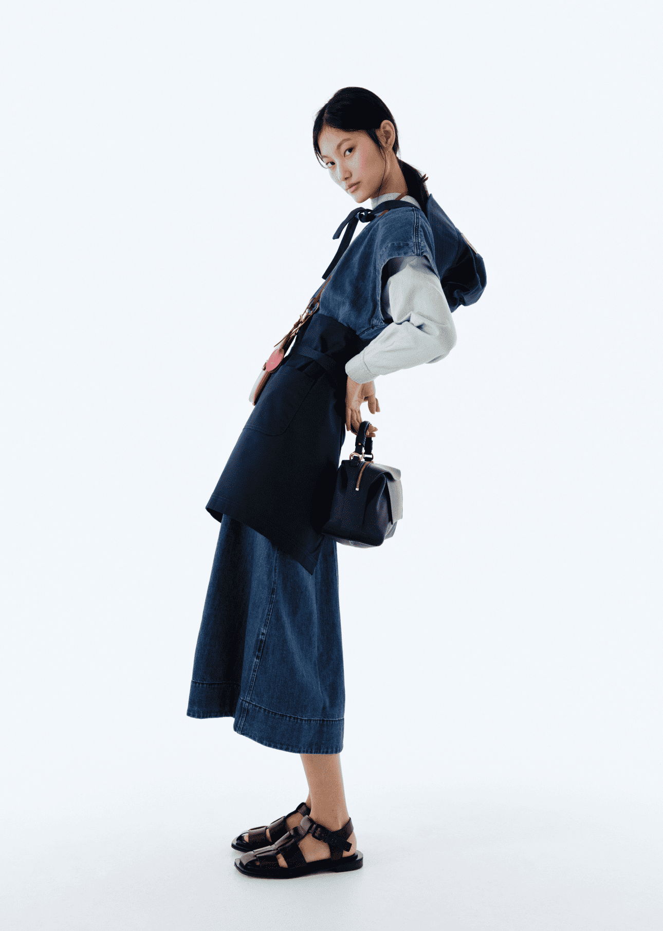 Model wearing denim outfit with a handbag, posing against a plain background.