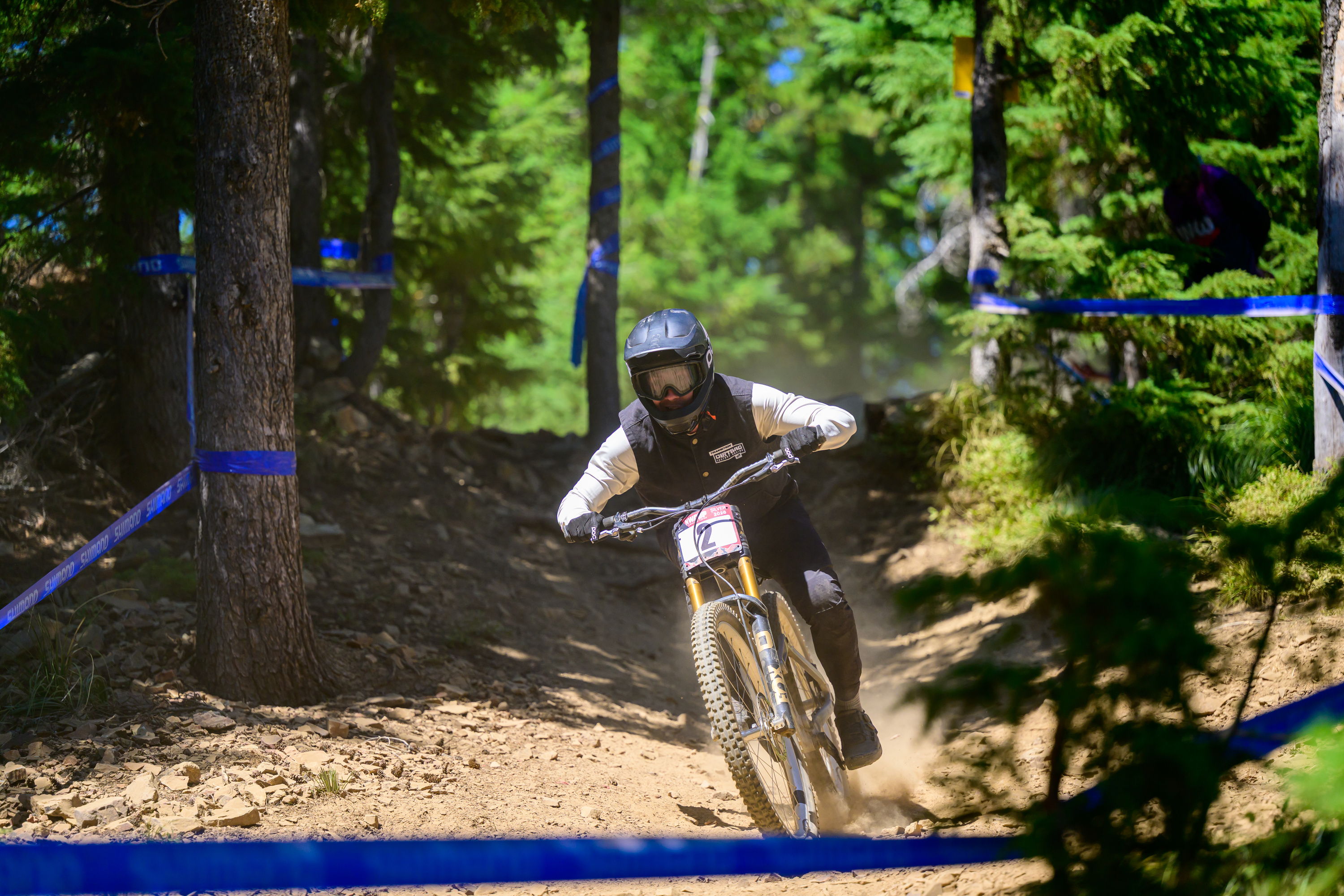 Mountain biker racing through a wooded trail with blue markers.