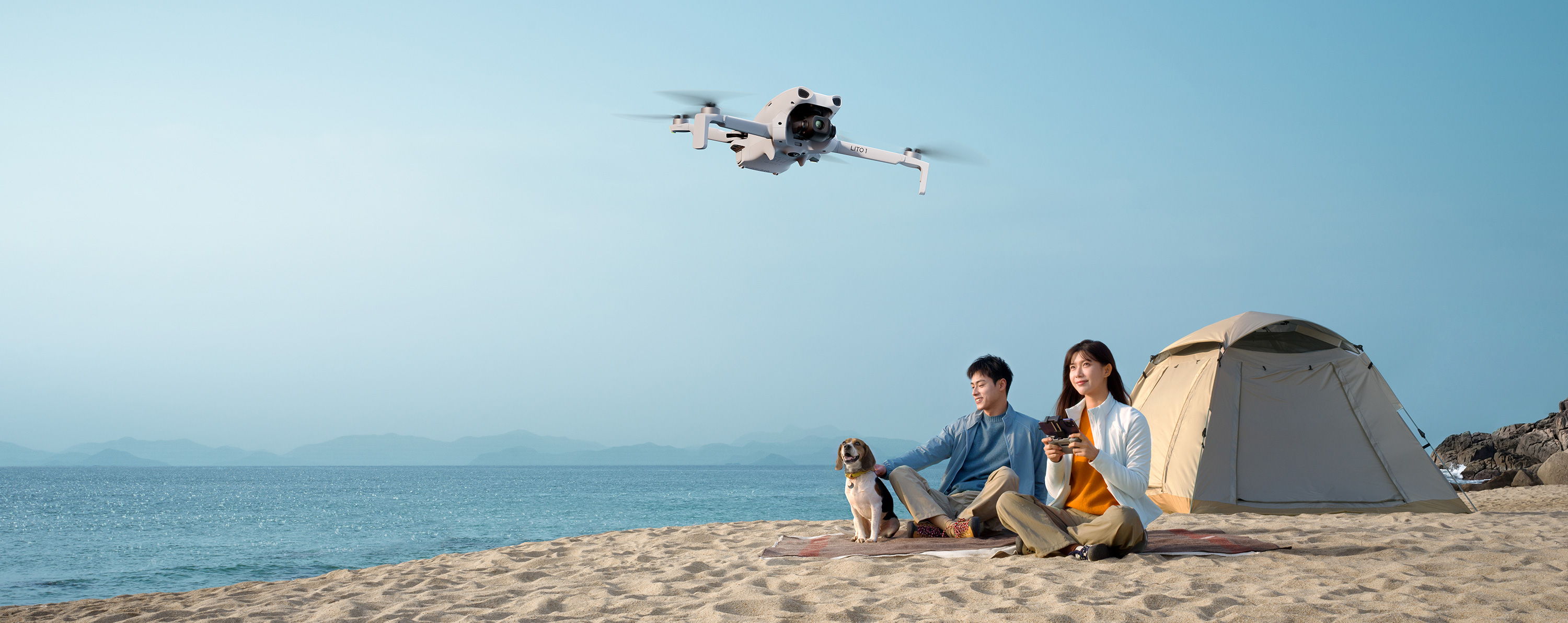 Family enjoying a beach day with a tent and dog, a DJI Lito 1 flies overhead