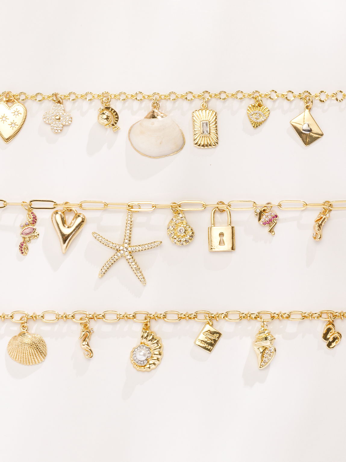 Gold charm necklaces featuring heart, starfish, shell, lock, and gemstone pendants displayed in layered rows.