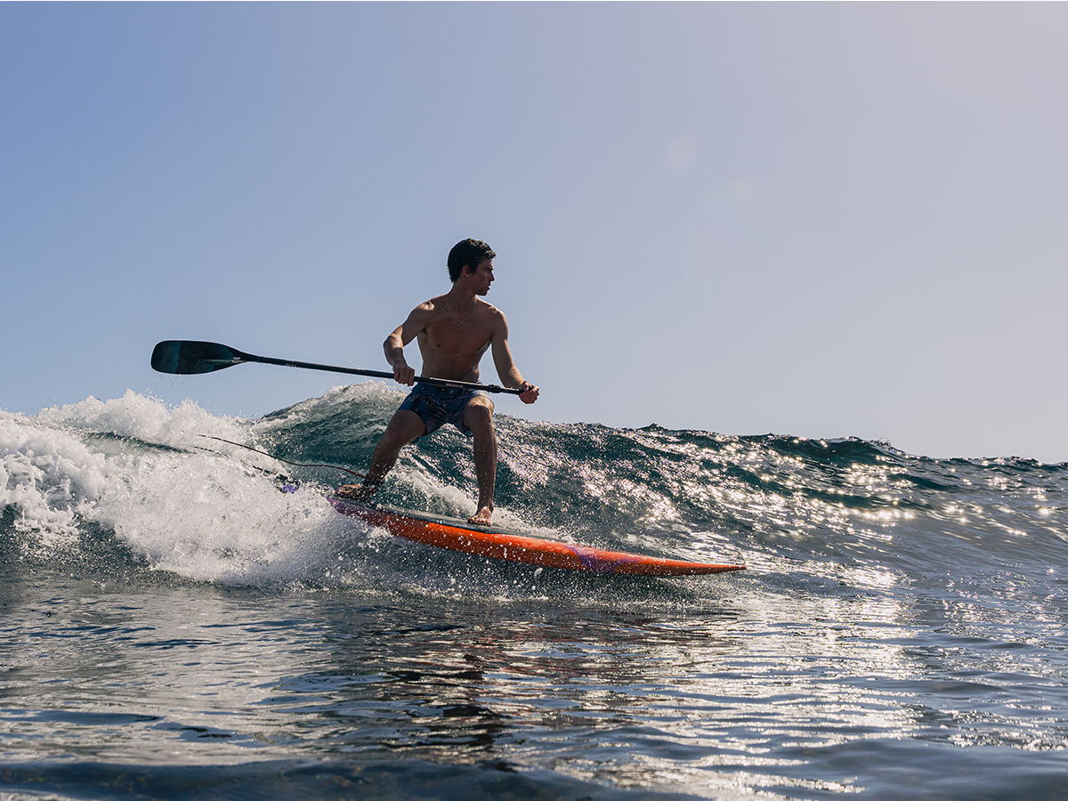 Person paddleboarding on a wave under a clear blue sky.