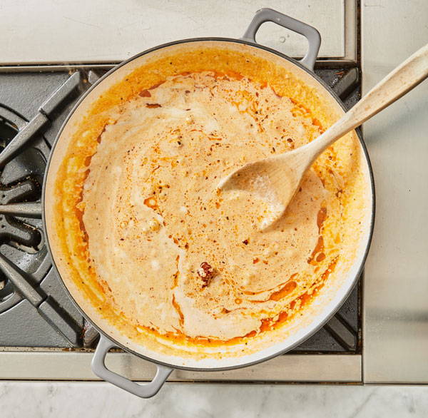 A creamy cheesy tomato pesto sauce cooking in a pan on the stove