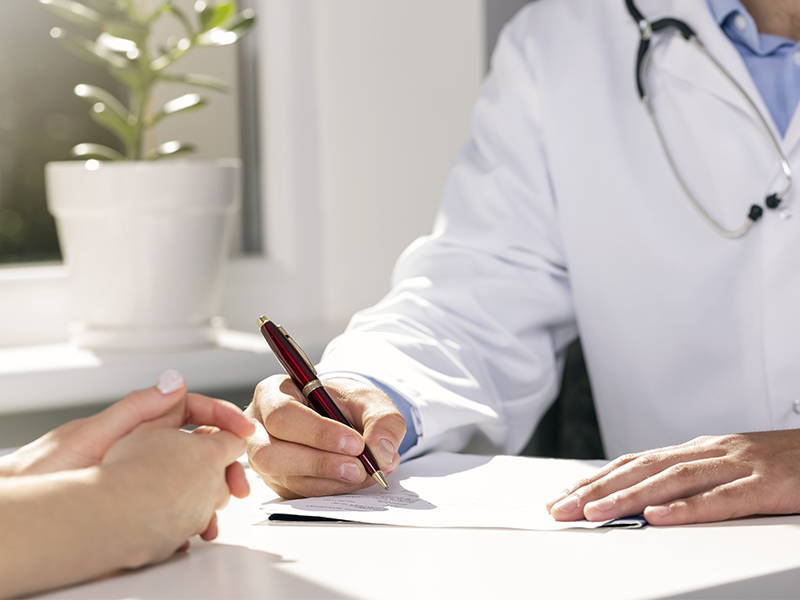 Een dokter aan tafel met een patiënt en schrijft wat op papier