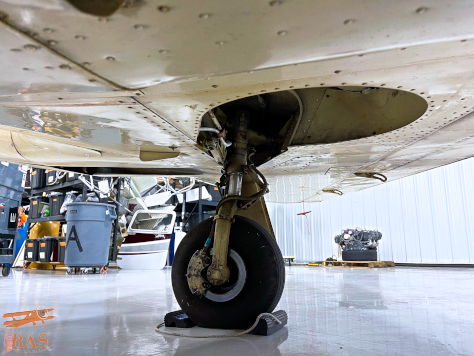 Close-up of an aircraft landing gear and wheel on a hangar floor.