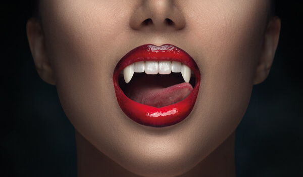 Woman with red lips and vampire fangs showing her tongue.