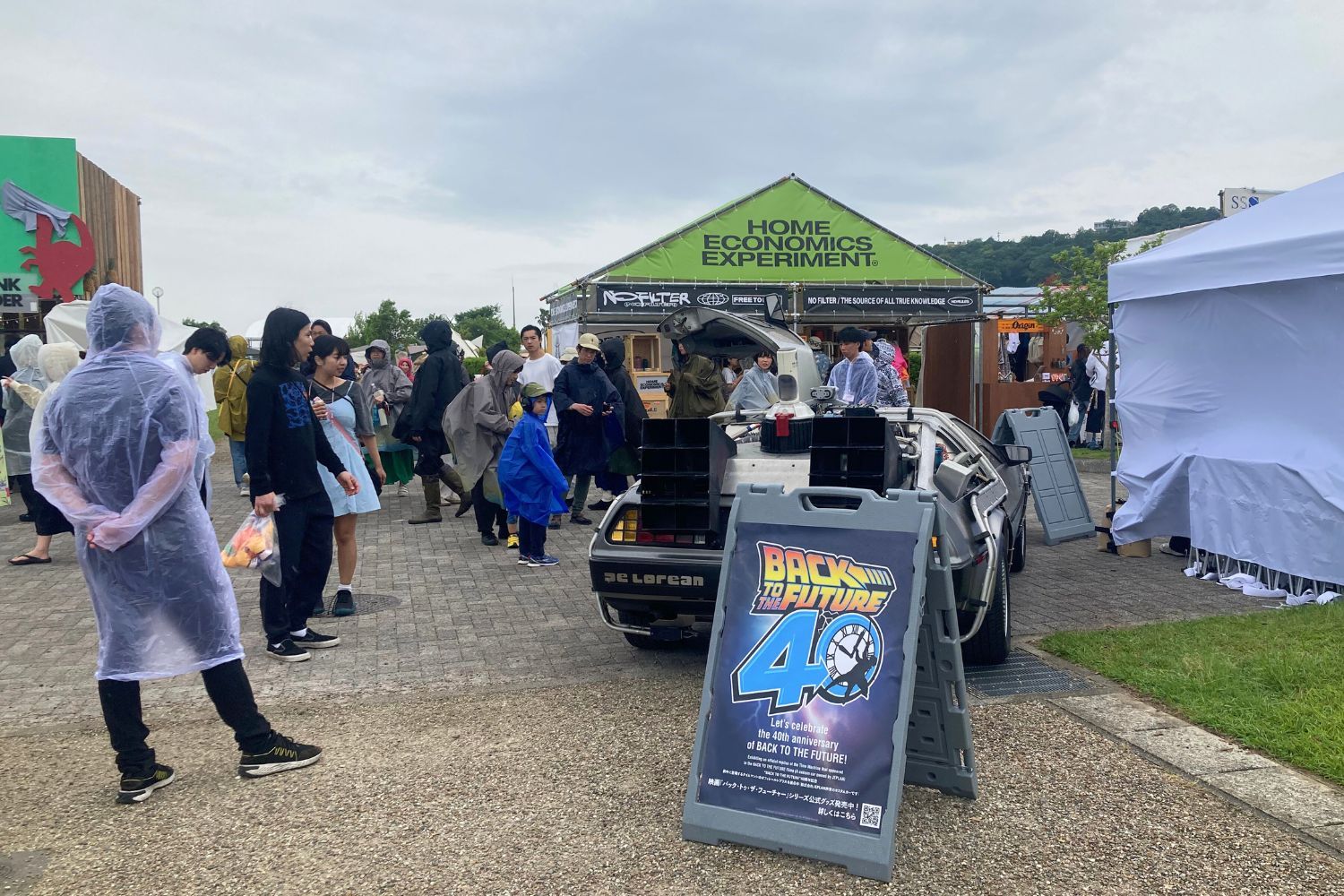 Crowd at an outdoor event with tents and a movie poster.